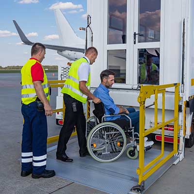 Airport ground staff assisting a wheelchair user to board an aircraft using a mobile lift.